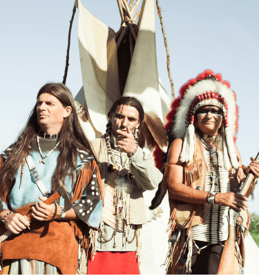 Nakota chiefs in traditional regalia beside tipis