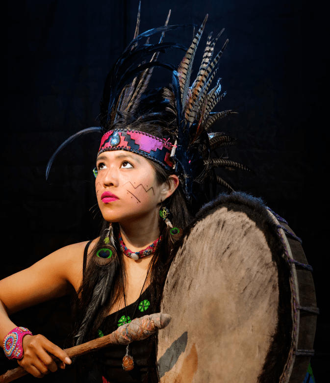 A Nakota dancer in traditional regalia playing a hand drum